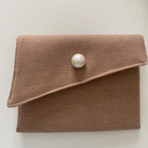 Può includere: Una pochette in feltro marrone con un solo bottone di perla.