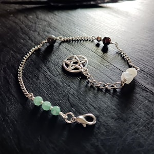 May include: Silver chain bracelet with a pentagram charm, green beads, and other gemstone accents. The bracelet has a lobster clasp closure and is displayed on a dark wooden surface.