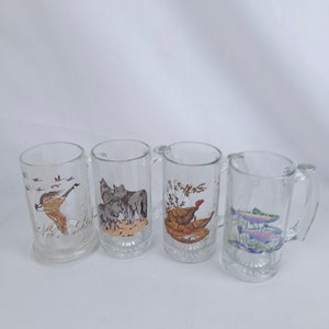 May include: Set of four clear glass mugs with handles. Each mug features a different nature-themed illustration: a flock of geese, a pack of wolves, a turkey, and a pair of trout.