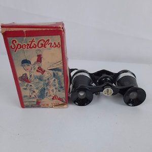 May include: A vintage box of black binoculars with a red and white illustration of a baseball player on the front. The box reads "Sports Glass New Type".