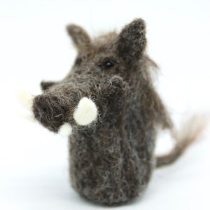 Könnte beinhalten: Ein braunes und graues Nadelfilz-Warzenschwein mit weißen Hauern. Das Warzenschwein steht auf einer weißen Oberfläche.