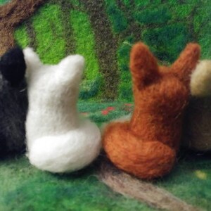 Puede incluir: Cuatro figuritas de animales de fieltro, un lobo negro y gris, un oso polar blanco, un zorro marr&oacute;n y un perro beige. Las figuritas est&aacute;n sentadas sobre una superficie de fieltro verde.
