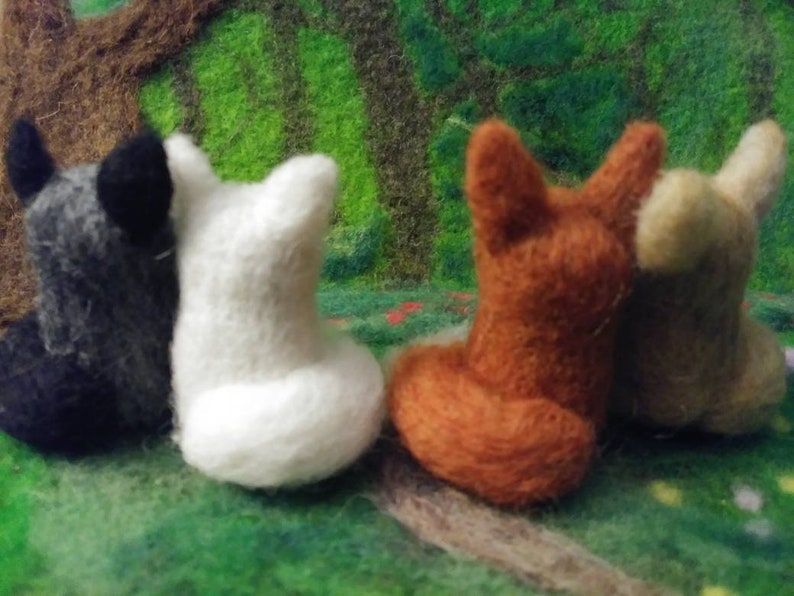 Puede incluir: Cuatro figuritas de animales de fieltro, un lobo negro y gris, un oso polar blanco, un zorro marr&oacute;n y un perro beige. Las figuritas est&aacute;n sentadas sobre una superficie de fieltro verde.