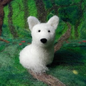 Puede incluir: Figurita de perro de fieltro de aguja blanca con ojos y nariz negros. La figurita est&aacute; sentada sobre un fondo verde y marr&oacute;n.