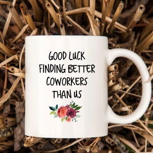 Peut inclure: Une tasse &agrave; caf&eacute; en c&eacute;ramique blanche avec du texte noir qui dit "Bonne chance pour trouver de meilleurs coll&egrave;gues que nous". La tasse a un motif floral avec des fleurs roses, rouges et vertes.