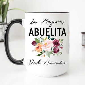May include: White ceramic mug with a black handle and black rim. The mug has a floral design and the text "La Mejor Abuelita Del Mundo" in black.