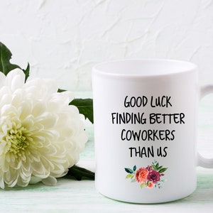 Peut inclure: Une tasse &agrave; caf&eacute; en c&eacute;ramique blanche avec du texte noir qui dit "Bonne chance pour trouver de meilleurs coll&egrave;gues que nous". La tasse a un motif floral avec des fleurs roses, rouges et blanches.