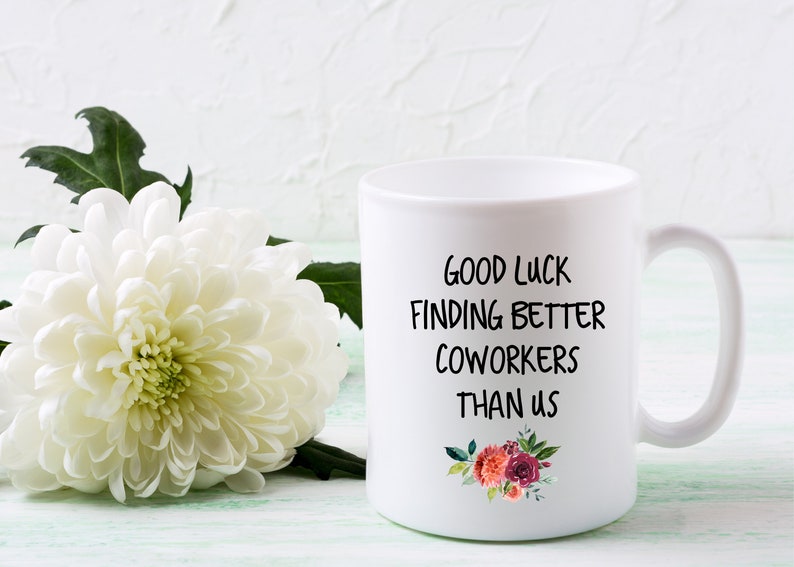Peut inclure: Une tasse &agrave; caf&eacute; en c&eacute;ramique blanche avec du texte noir qui dit "Bonne chance pour trouver de meilleurs coll&egrave;gues que nous". La tasse a un motif floral avec des fleurs roses, rouges et blanches.