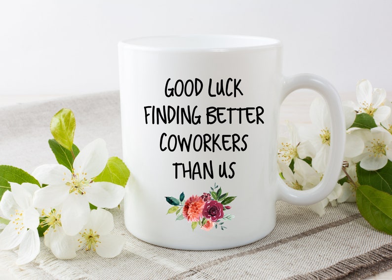 Peut inclure: Une tasse &agrave; caf&eacute; en c&eacute;ramique blanche avec du texte noir qui dit "Bonne chance pour trouver de meilleurs coll&egrave;gues que nous". La tasse a un motif floral avec des fleurs roses et rouges.