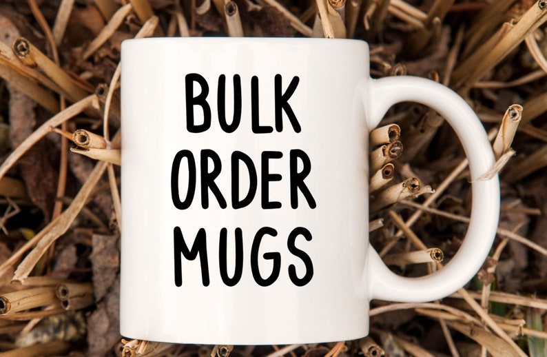 May include: White ceramic mug with black text that reads "BULK ORDER MUGS". The mug is sitting on a bed of dried brown grass.