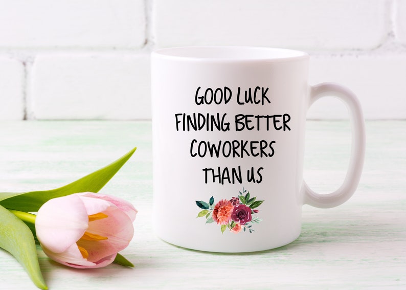 Peut inclure: Une tasse &agrave; caf&eacute; en c&eacute;ramique blanche avec du texte noir qui dit "Bonne chance pour trouver de meilleurs coll&egrave;gues que nous". La tasse a un motif floral avec des fleurs rouges, roses et orange.