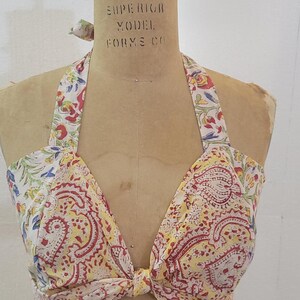 May include: A vintage halter top with a paisley print in shades of yellow, red, and blue. The top is tied at the front and has a halter neck.