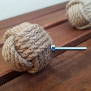 May include: A close-up of a brown rope cabinet knob with a silver metal screw. The knob is tied in a knot and is a decorative accent for a cabinet or drawer.