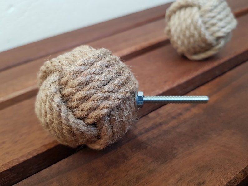 May include: A close-up of a brown rope cabinet knob with a silver metal screw. The knob is tied in a knot and is a decorative accent for a cabinet or drawer.