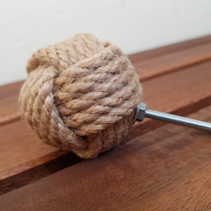 Op de afbeelding: Een bruine touwknop met een zilveren metalen schroef. De knop is in een knoop geknoopt en is een decoratief hardware-onderdeel.