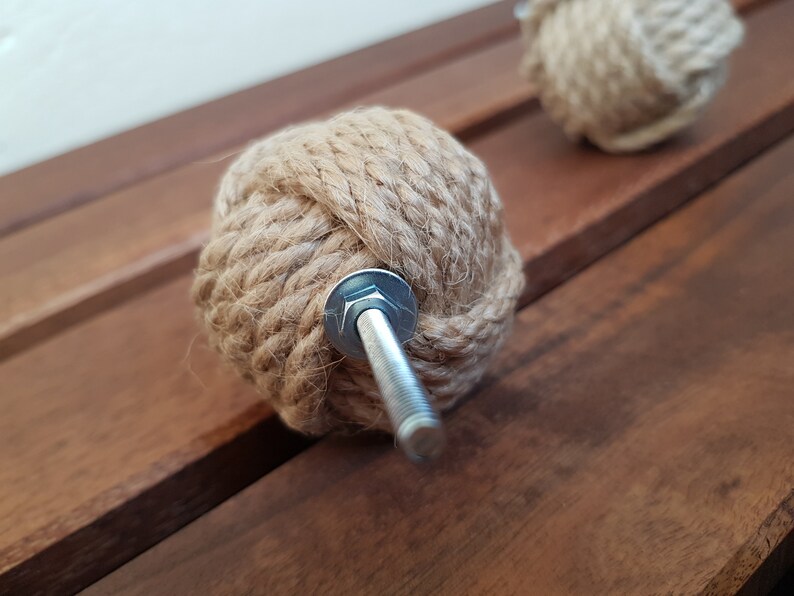 May include: A close-up of a brown rope knob with a silver screw. The knob is made of natural rope and has a knot design. It is a decorative hardware piece for furniture or cabinets.