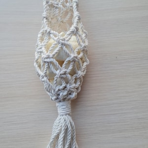 May include: A cream-coloured macrame plant hanger. It has a wooden ring at the top, a woven net body, and a tassel at the bottom. The plant holder is made from cotton. The design is simple and elegant, suitable for indoor plants.