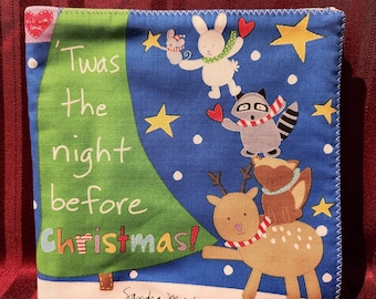 Pode incluir: Decoração quadrada de tecido com tema natalino com fundo azul apresentando uma árvore de Natal verde e animais de desenho animado. O texto "'Twas the night before Christmas!" é exibido. A decoração tem uma borda branca e é assinada "Sandra Magsamen."
