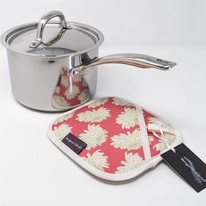 May include: A stainless steel saucepan with a lid and a floral print pot holder. The pot holder has a white background with pink flowers and a tag that says "Margaret Clavell".
