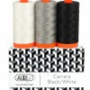 May include: Three spools of thread in white, gray, and black with orange tops. The spools are in a box with a black and white geometric pattern and the text "Laura Ashley Cotton Black Threads".