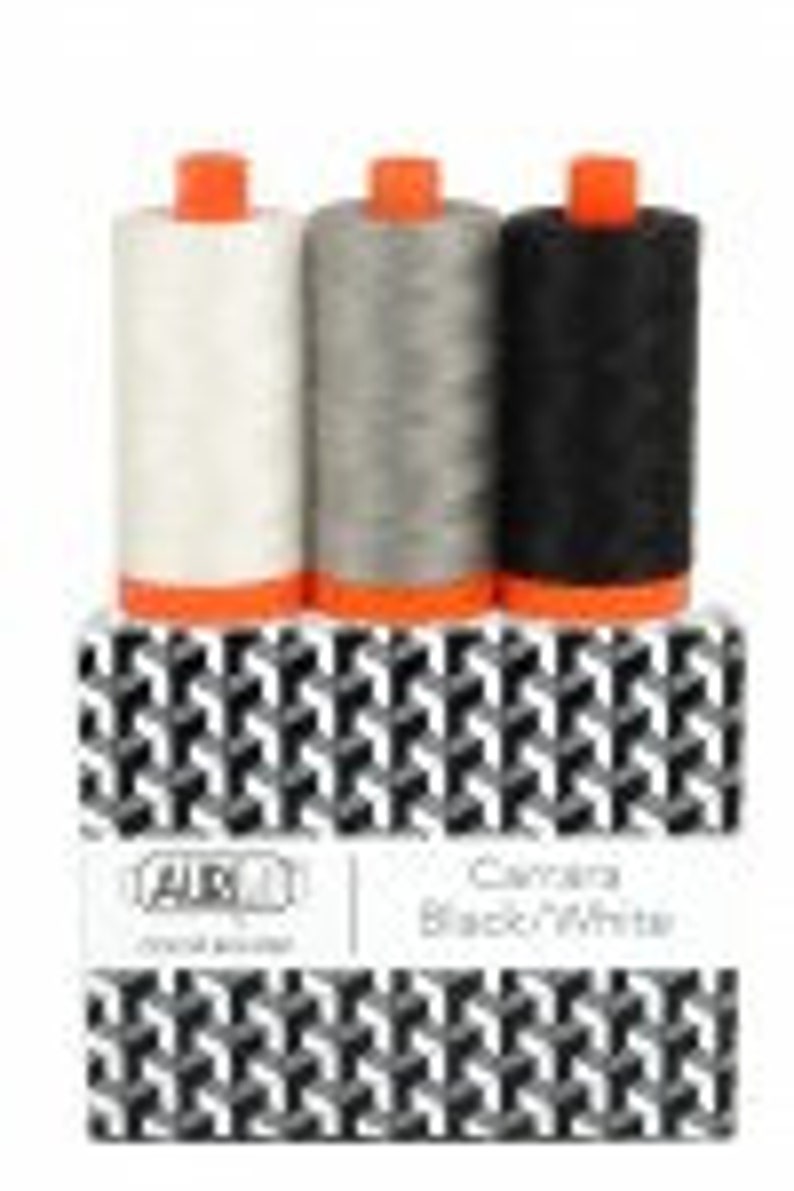May include: Three spools of thread in white, gray, and black with orange tops. The spools are in a box with a black and white geometric pattern and the text "Laura Ashley Cotton Black Threads".