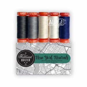 May include: A set of four spools of 100% cotton thread in shades of gray, white, and blue. The spools are labeled "Aurifil Made" and "100% Cotton". The set is packaged in a box with a map of New York City and the text "The Tattooed Quilter New York Neutrals".