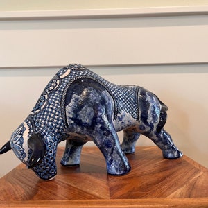 May include: A blue and white ceramic bull figurine with intricate patterns. The bull is standing on a wooden surface.