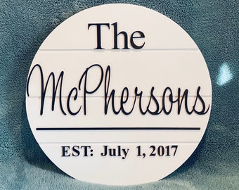 May include: White round wooden sign with black text that reads "The McPhersons EST: July 1, 2017".