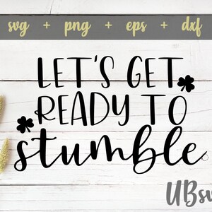 May include: Black and white text on a white wood background that reads "Let's Get Ready To Stumble". There are two shamrock symbols on either side of the text.