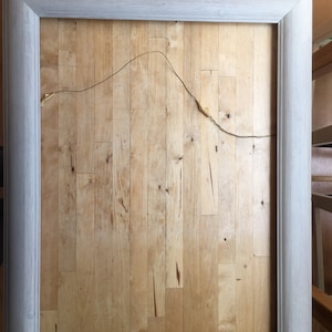 May include: A white wood picture frame with a simple, clean design. The frame is lying flat on a wooden surface.