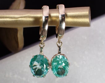 May include: A pair of gold hoop earrings with a dangling oval-shaped turquoise gemstone.