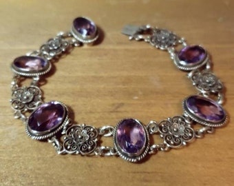 May include: A silver bracelet with a delicate filigree design and oval-shaped amethyst gemstones.