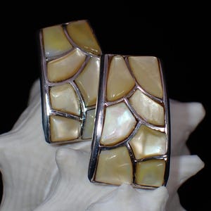 Puede incluir: Un par de pendientes de plata con un diseño geométrico. Los pendientes están hechos de nácar y tienen un color amarillo claro.