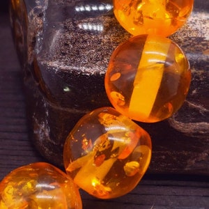 May include: A strand of amber beads, each bead is a different shade of orange and has a translucent quality. The beads are round and smooth.