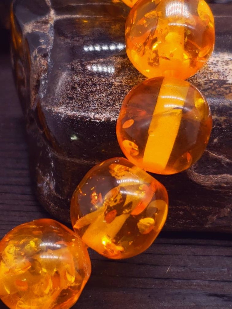 May include: A strand of amber beads, each bead is a different shade of orange and has a translucent quality. The beads are round and smooth.
