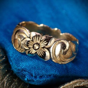 Può includere: Un anello d'argento con un design floreale. L'anello è su uno sfondo blu.