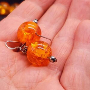 May include: A pair of amber earrings with silver hooks. The amber is a deep orange colour and has a speckled pattern.