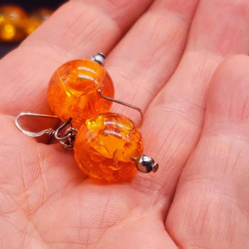 May include: A pair of amber earrings with silver hooks. The amber is a deep orange colour and has a speckled pattern.