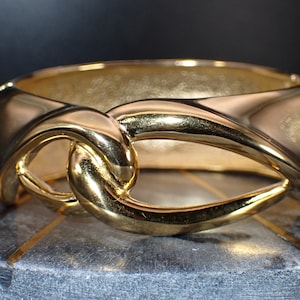 Puede incluir: Un brazalete dorado con un diseño de nudo retorcido.