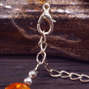 May include: A silver chain necklace with a lobster clasp and amber beads. The beads are round and have a mottled orange colour.