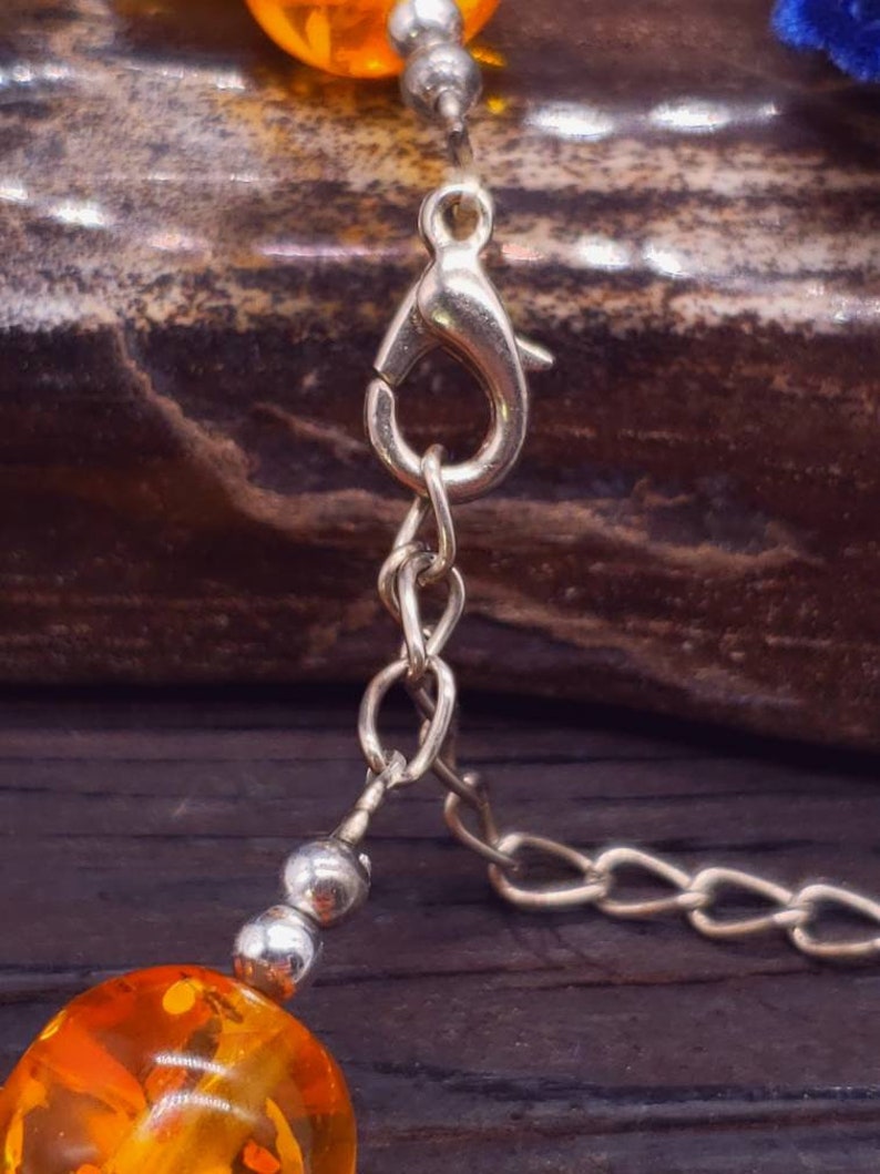 May include: A silver chain necklace with a lobster clasp and amber beads. The beads are round and have a mottled orange colour.