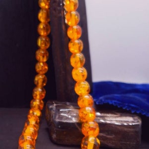 May include: A necklace made of round, amber-coloured beads. The beads are strung on a silver chain and are arranged in a simple, elegant design.