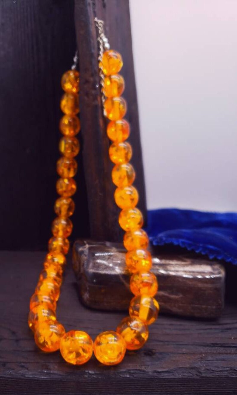 May include: A necklace made of round, amber-coloured beads. The beads are strung on a silver chain and are arranged in a simple, elegant design.