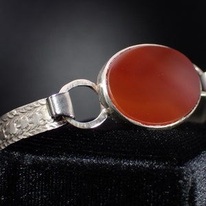 May include: A silver bracelet with an oval carnelian stone. The bracelet has a delicate floral design.