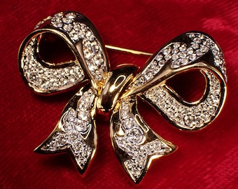 May include: A gold-toned bow brooch with clear rhinestones. The bow is tied in a knot with two loops and a pointed end.