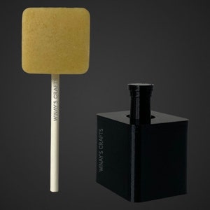 May include: A square lollipop with a yellow candy on a white stick. The stick has the text "WINAY'S CRAFTS" printed on it. The lollipop is next to a black square mold with the same text printed on it.
