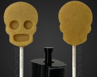 May include: Two sugar skull lollipops with white sticks, one with an outline and one without. A black plastic mold for making the lollipops is also shown. The mold has the text "Winay's Crafts" on it.