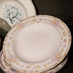 May include: A set of white ceramic bowls with a floral design. The bowls have a gold rim and a delicate floral pattern in shades of pink, yellow, and blue.