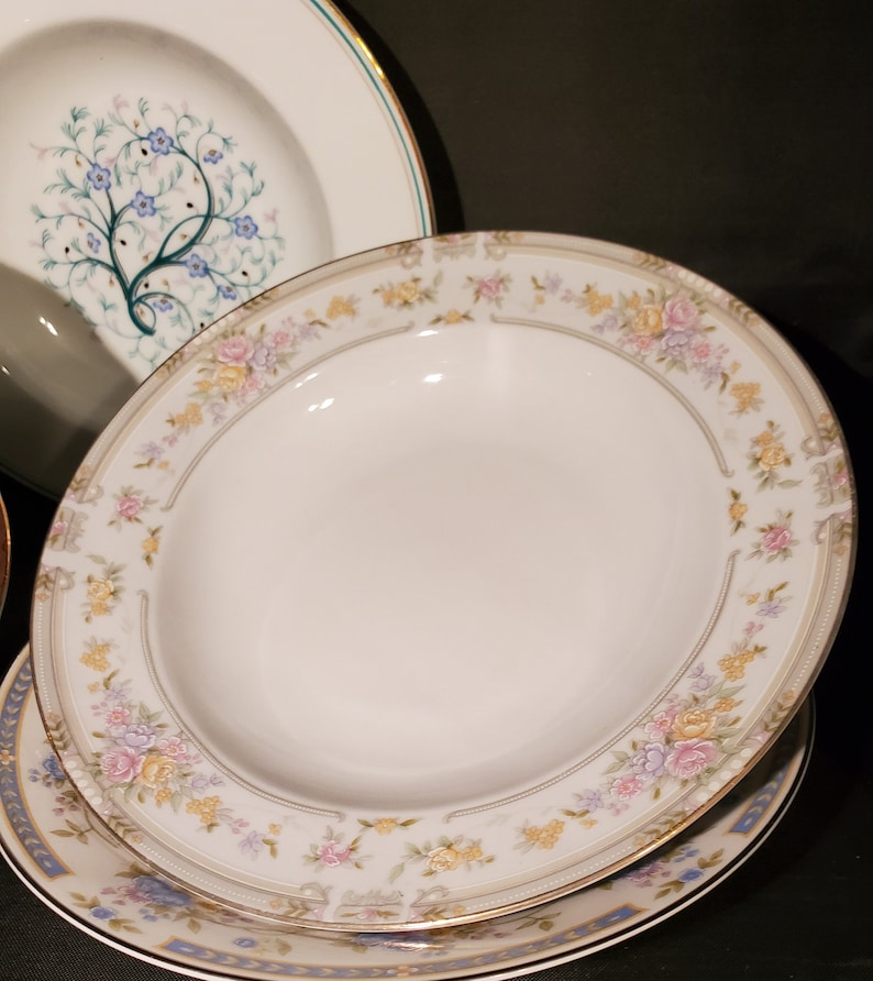 May include: A set of white ceramic bowls with a floral design. The bowls have a gold rim and a delicate floral pattern in shades of pink, yellow, and blue.