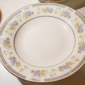 May include: A white ceramic soup bowl with a blue and gold floral pattern around the rim.